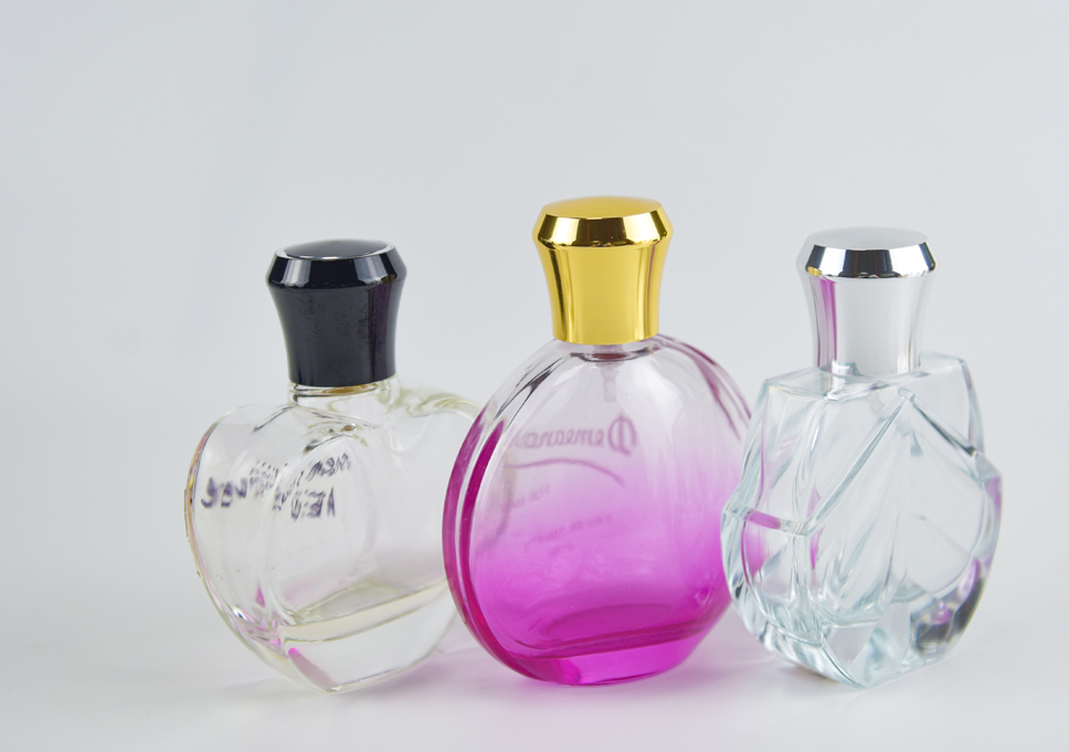Black, gold and silver tapered metal perfume caps on clear and pink glass bottles against a light gray background